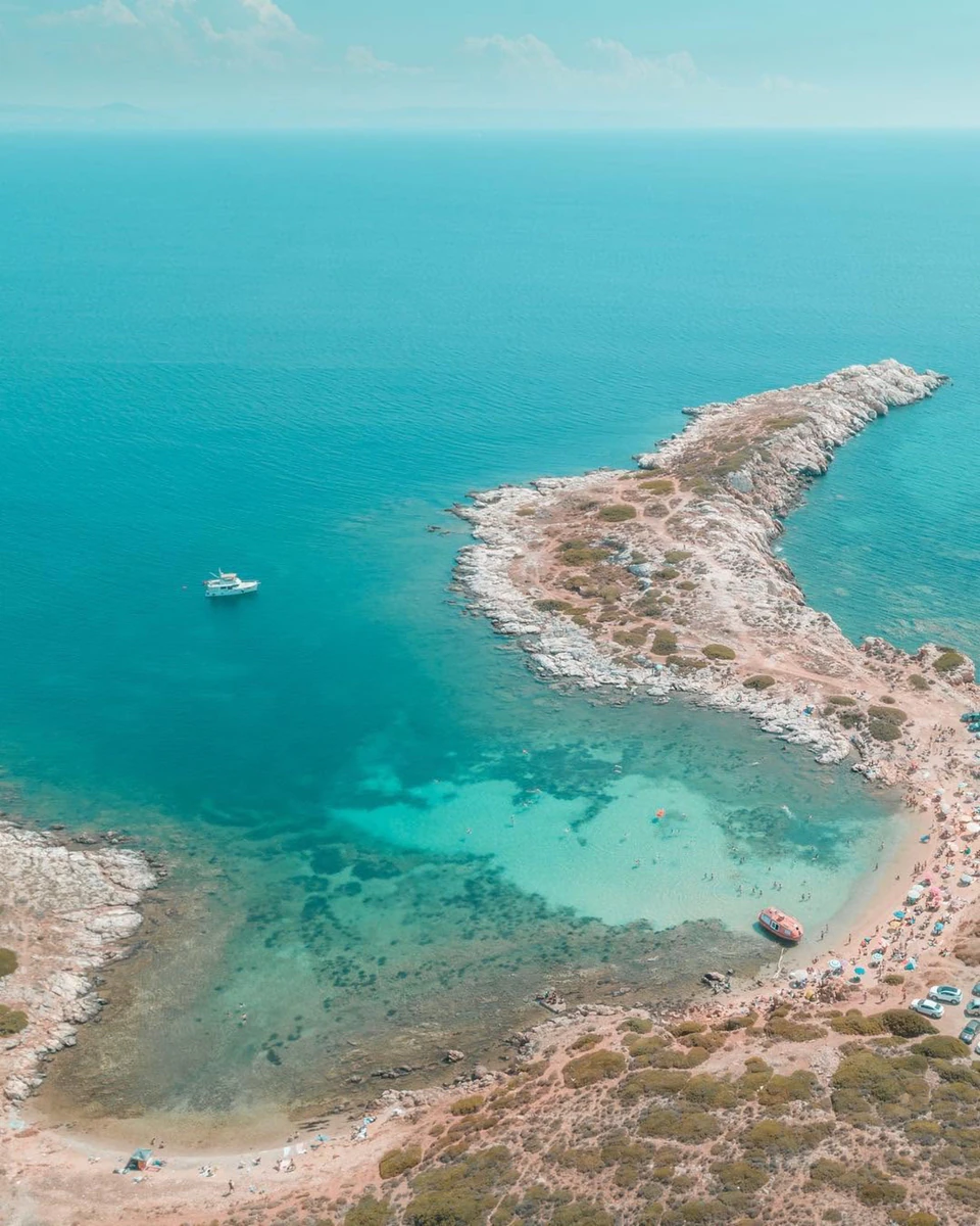 A lone boat anchored off a rocky spit in glass-clear turquoise water
