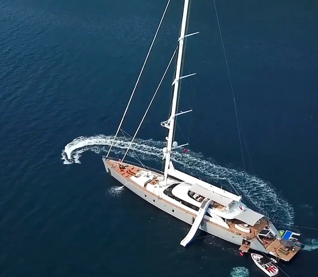 A white 50-metre sailing yacht with a waterslide and open stern beach club