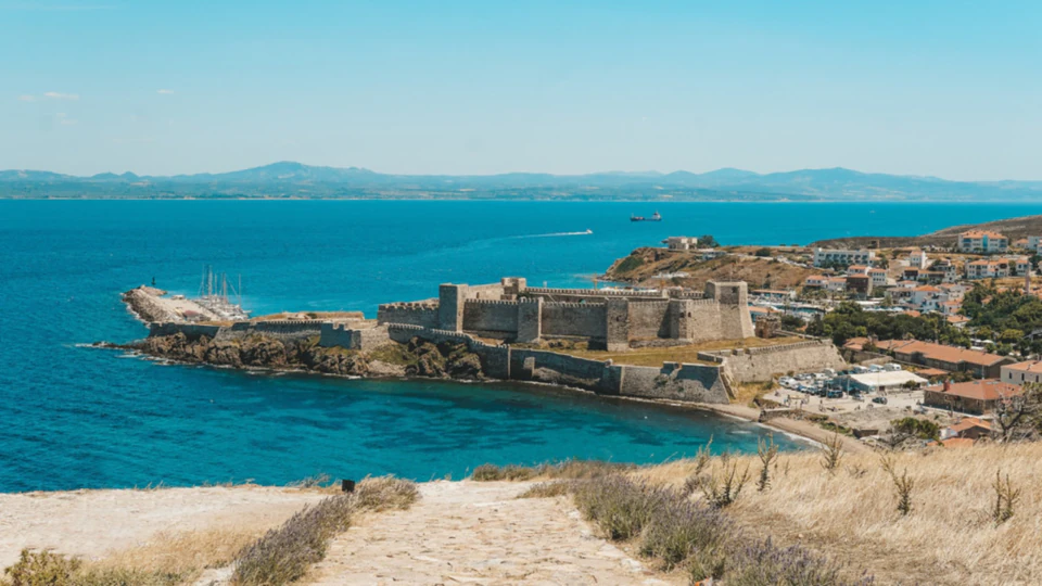Bozcaada's fortress and harbour across turquoise water, seen from the dunes