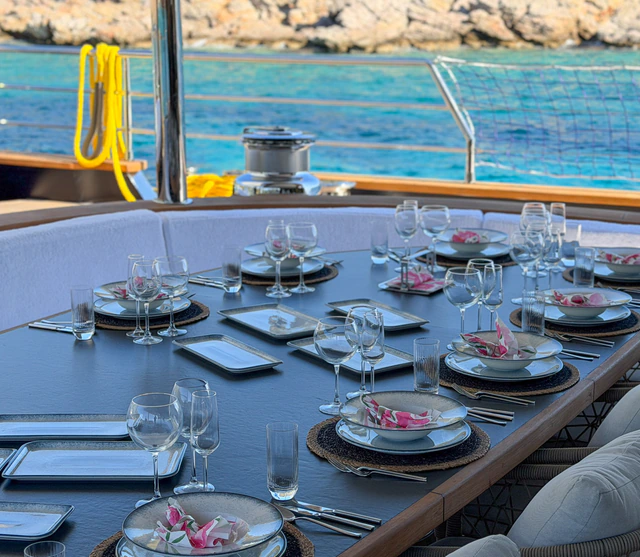 An elegant onboard dining table set with flowers, crystal glasses and fine tableware overlooking turquoise water